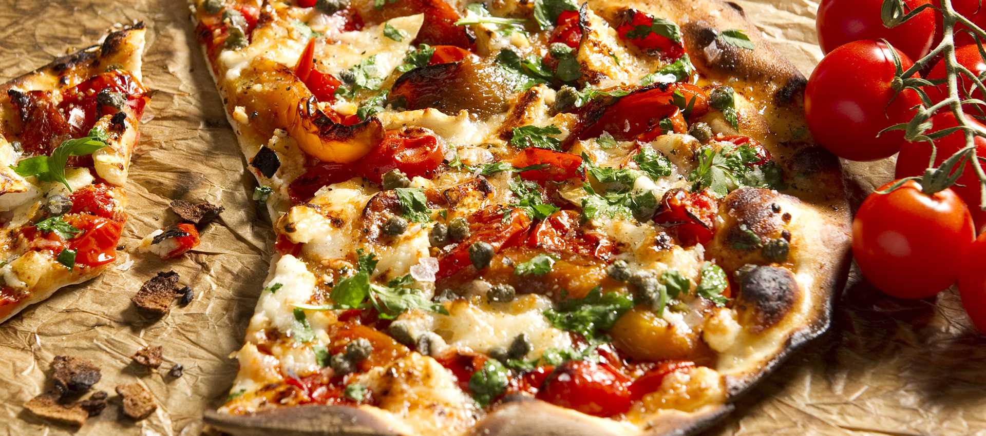 Pizza with tomatoes, goat cheese, bell peppers, capers and herbs